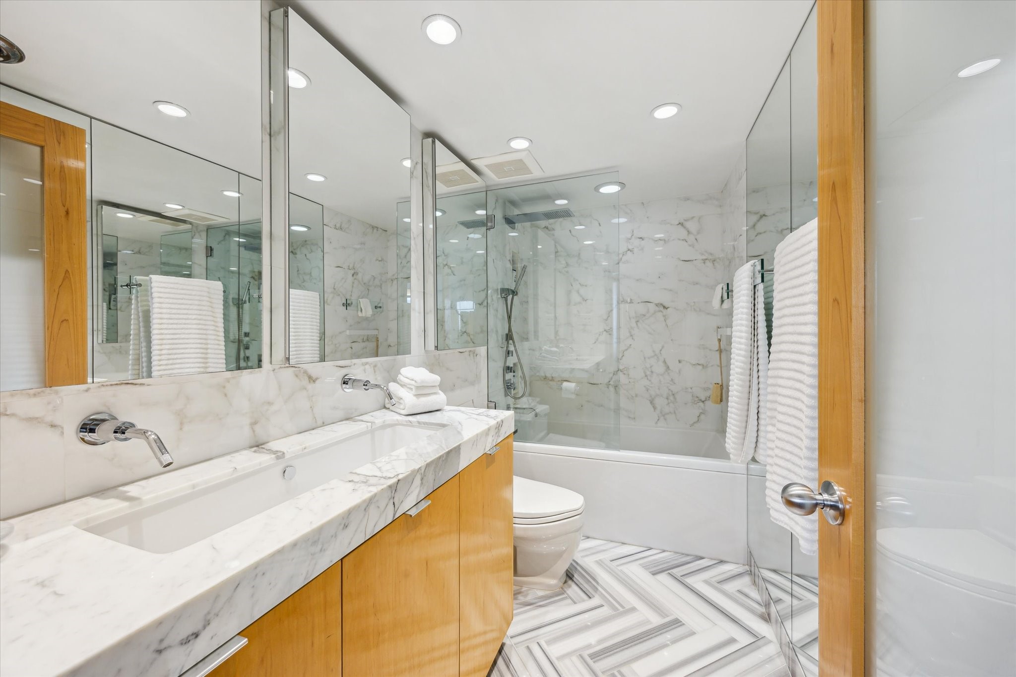 2701 Westheimer Road, Unit 9E Houston, TX 77098 - Photo 14 of 31 This spa-inspired bathroom is designed for ultimate relaxation, featuring a generously sized sink complete with two adjustable faucets for precise water control. The design incorporates a marble counter, backsplash, and herringbone design flooring. Three medicine cabinets outfitted with outlets and ambien lighting.