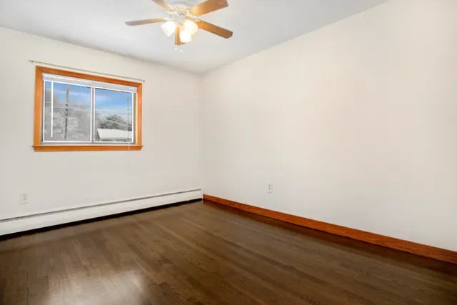 a view of an empty room with wooden floor and a ceiling fan