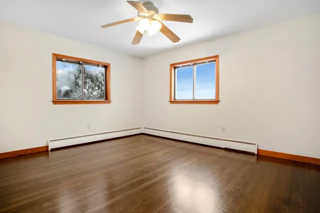 a view of an empty room with wooden floor and a ceiling fan