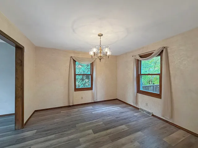 an empty room with wooden floor chandelier and windows