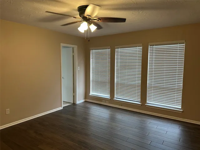 an empty room with wooden floor fan and windows