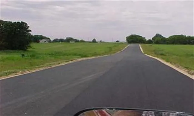 a view of a street with a big yard and a large trees
