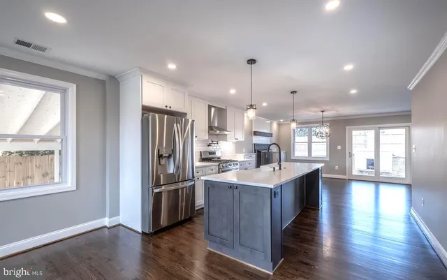 a kitchen with stainless steel appliances granite countertop a refrigerator a sink dishwasher a stove and a dining table with wooden floor