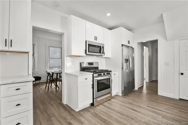 a kitchen with stainless steel appliances white cabinets a sink a stove a refrigerator and microwave with wooden floor