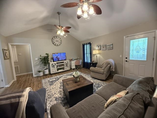 395 Austin Street Savannah, TN 38372 - Photo 4 of 32 Vaulted ceiling living area featuring wood-finish flooring, two ceiling fans with integrated lighting, a white entry door with decorative glass inlay, and a doorway opening to an additional room
