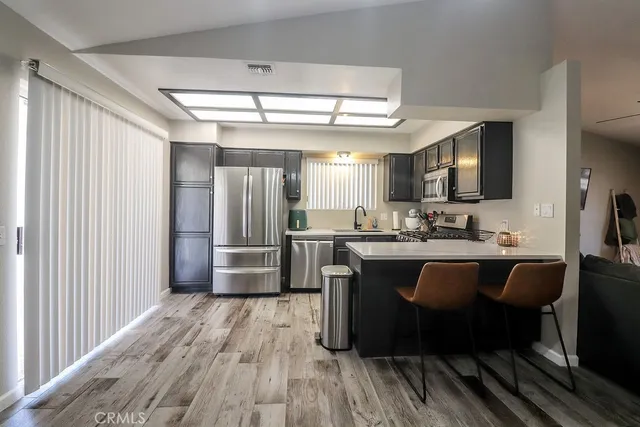a kitchen with stainless steel appliances kitchen island granite countertop a refrigerator a sink dishwasher a stove and a dining table with wooden floor