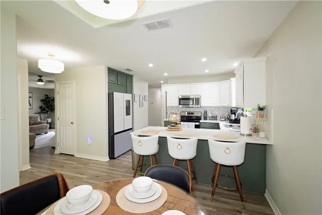 a living room with stainless steel appliances a dining table wooden floor and a view of kitchen