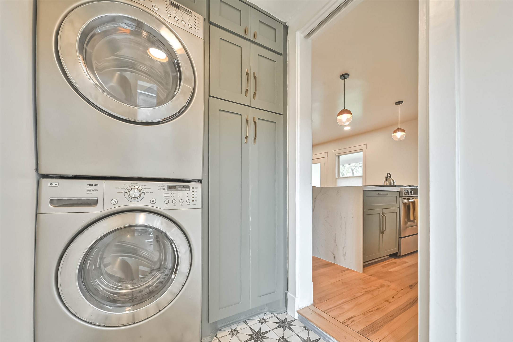 412 Sue Street Houston, TX 77009 - Photo 9 of 19 In house utility room, with a stacked washer and dryer, adjacent to a modern kitchen featuring sleek cabinetry, pendant lighting, and pattern tile flooring.