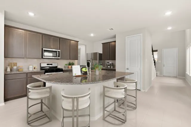 a kitchen with stainless steel appliances granite countertop a stove a sink a refrigerator a dining table and chairs