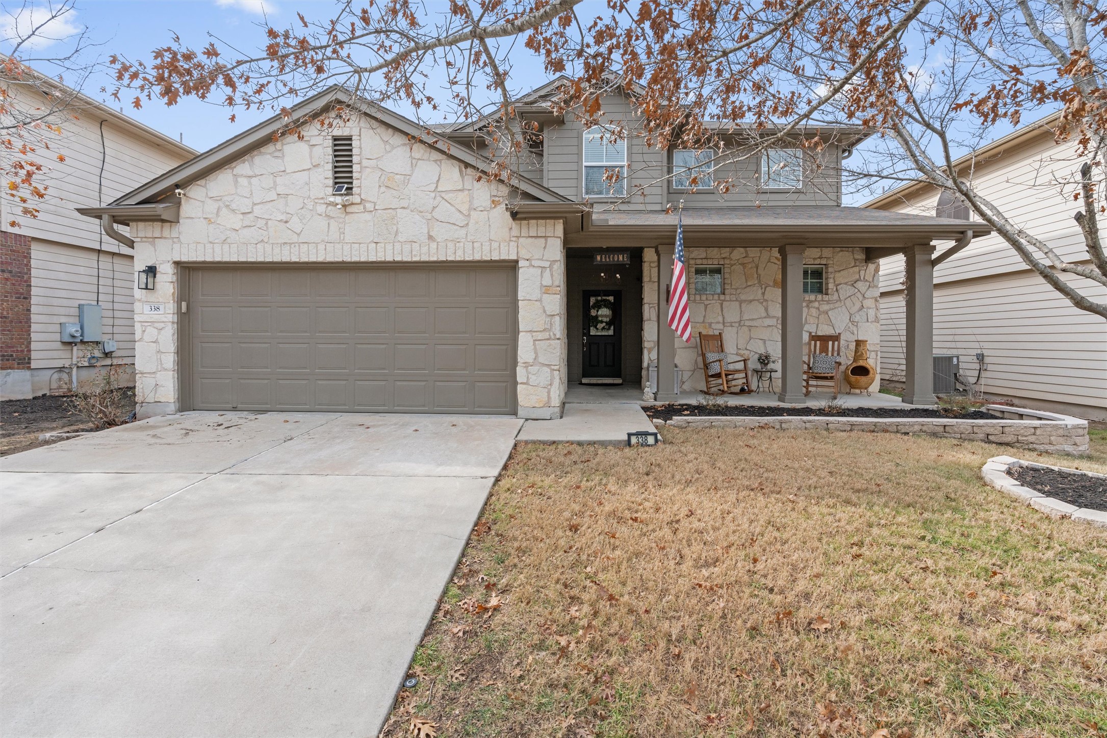 View of front of property featuring covered porch, stone siding, driveway, an attached garage, and a front yard
