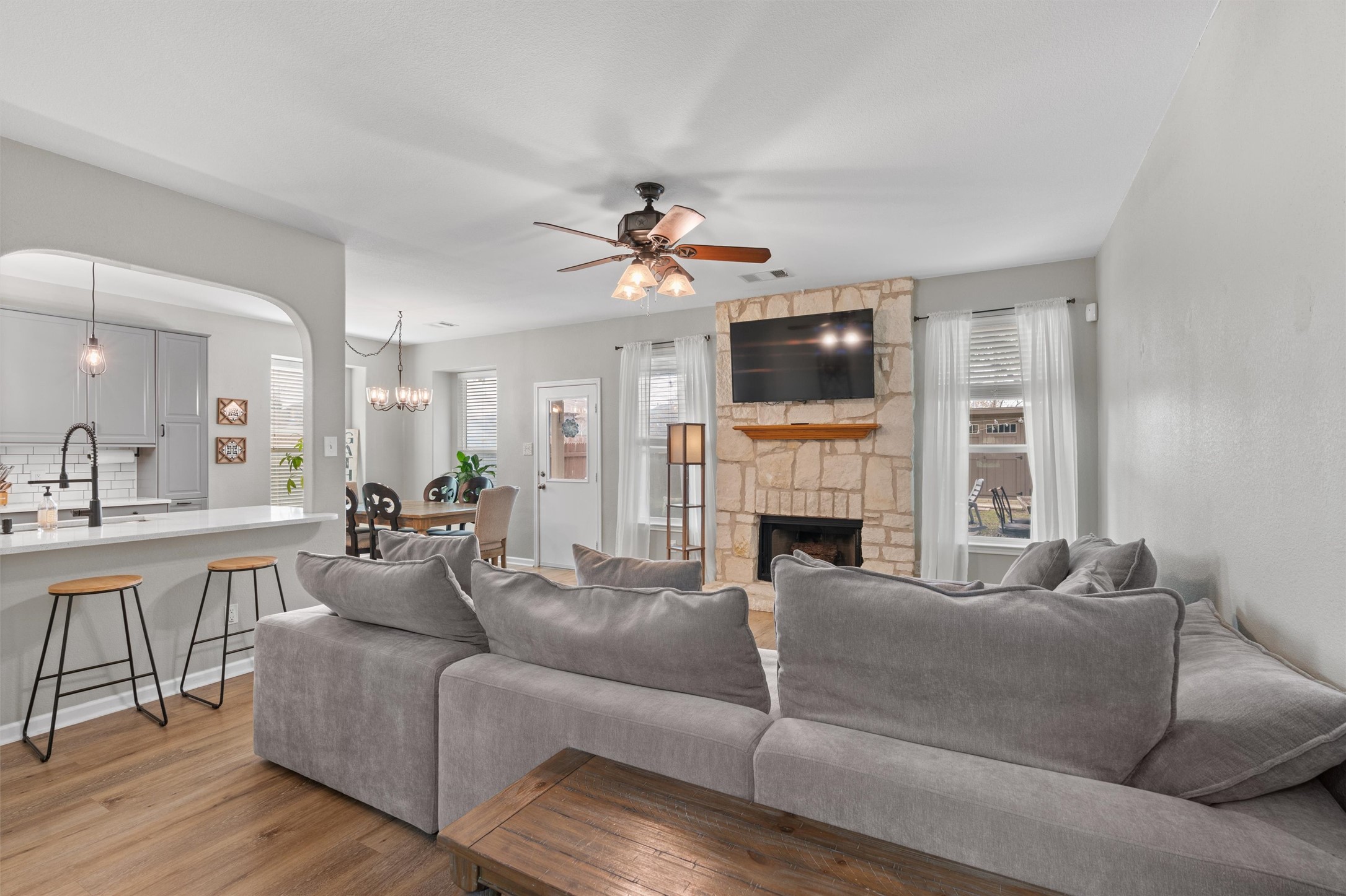 338 Altamont Street Hutto, TX 78634 - Photo 6 of 40 Living area featuring a ceiling fan, light wood-type flooring, arched walkways, a stone fireplace, and hanging lights