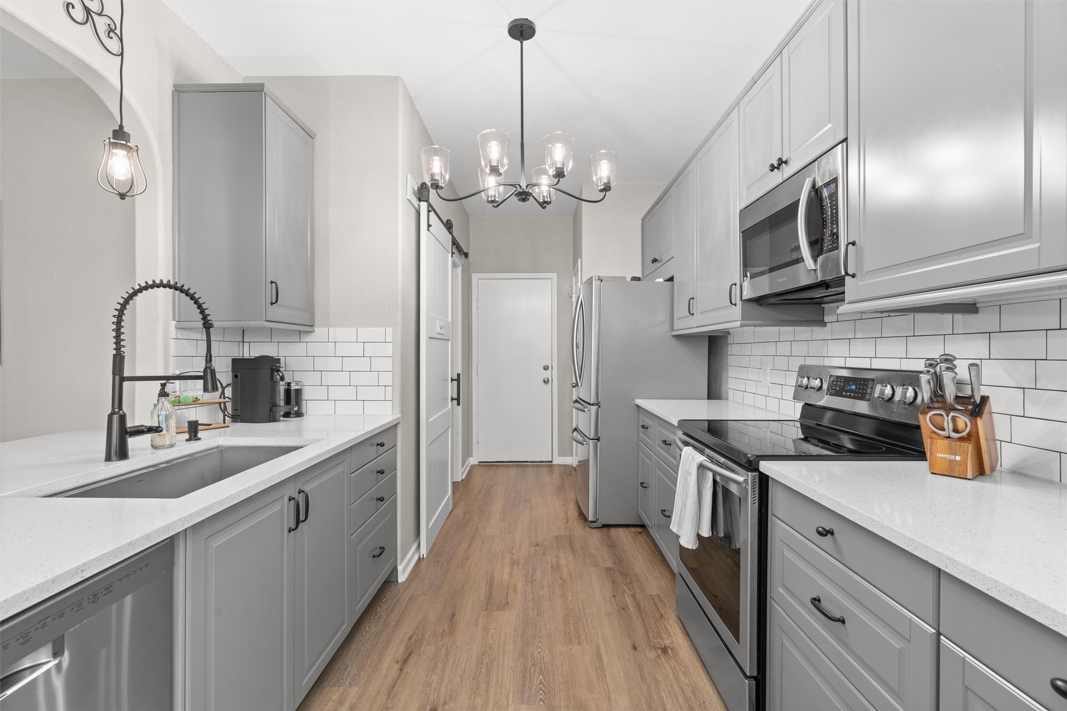 338 Altamont Street Hutto, TX 78634 - Photo 10 of 40 Kitchen with gray cabinets, stainless steel appliances, light wood-style floors, light stone counters, and a barn door