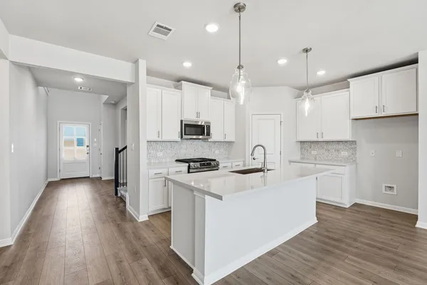 a large kitchen with stainless steel appliances granite countertop a stove a sink a refrigerator and white cabinets with wooden floor