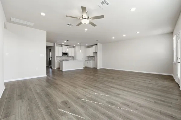 a view of an empty room and kitchen view with wooden floor