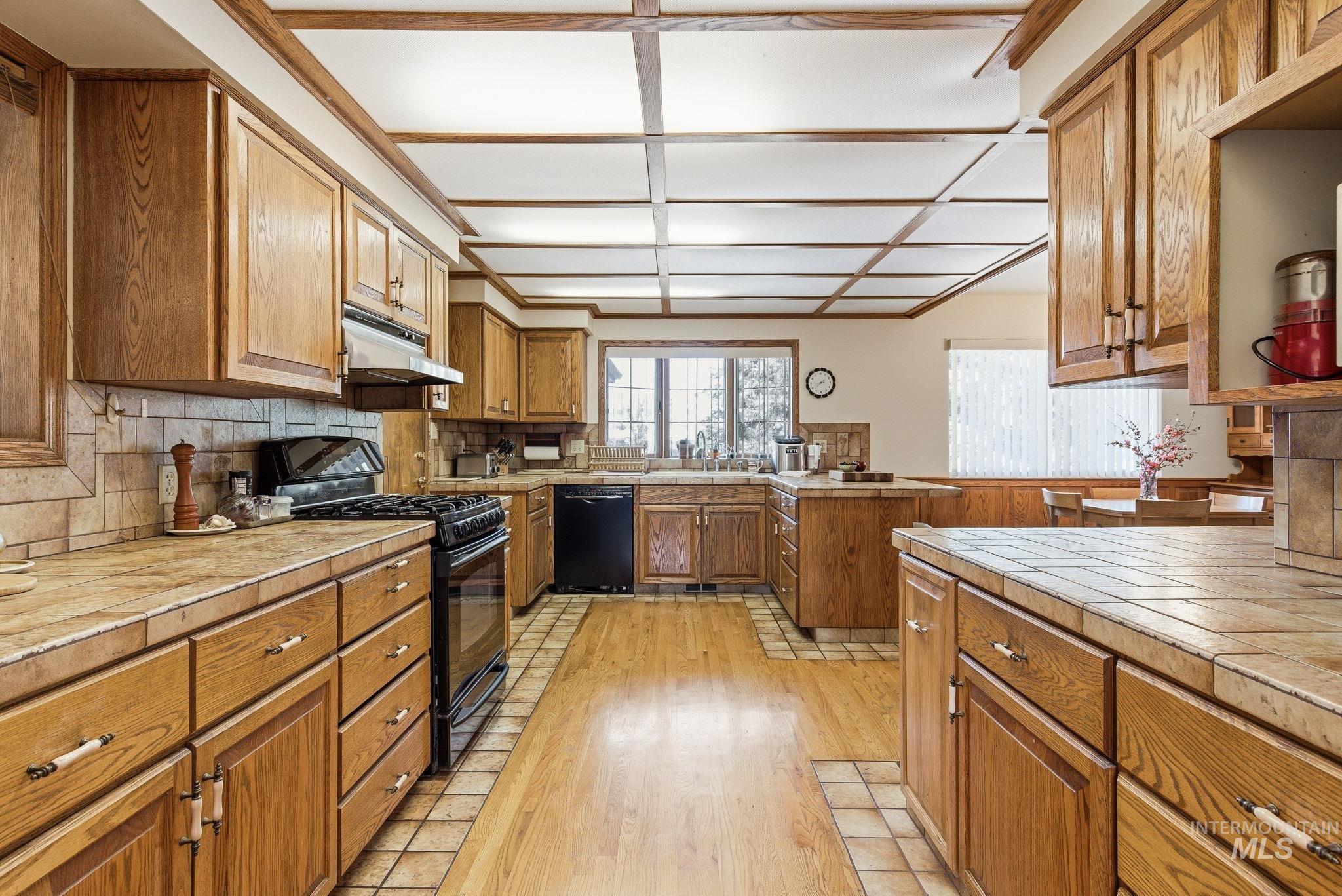 12055 West McMillan Road Boise, ID 83713 - Photo 11 of 42 Kitchen featuring tile countertops, black appliances, light wood finished floors, wood finish cabinetry, and tasteful backsplash