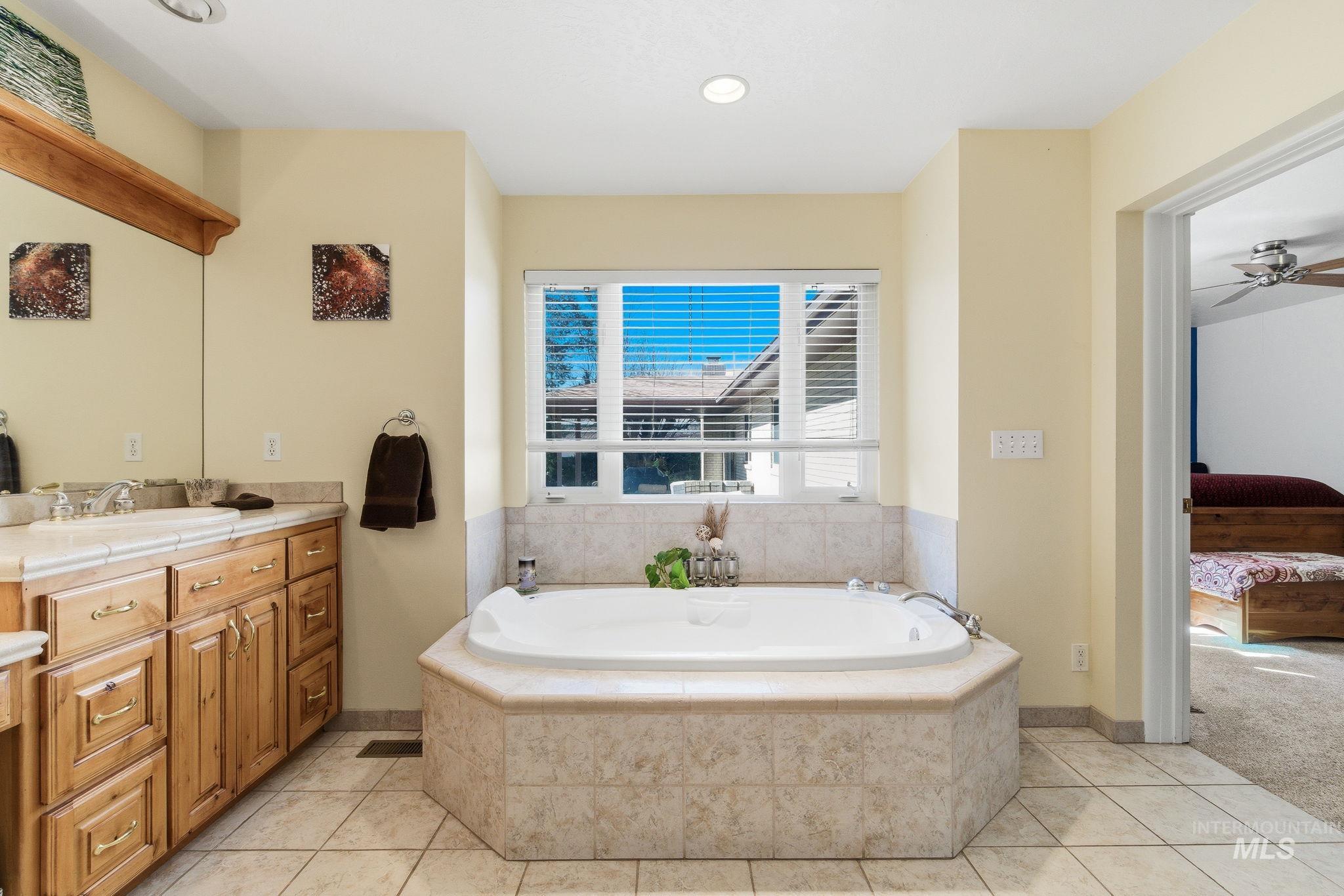 12055 West McMillan Road Boise, ID 83713 - Photo 16 of 42 Full bath with ensuite bathroom, vanity, a garden tub, light tile patterned floors, and a ceiling fan