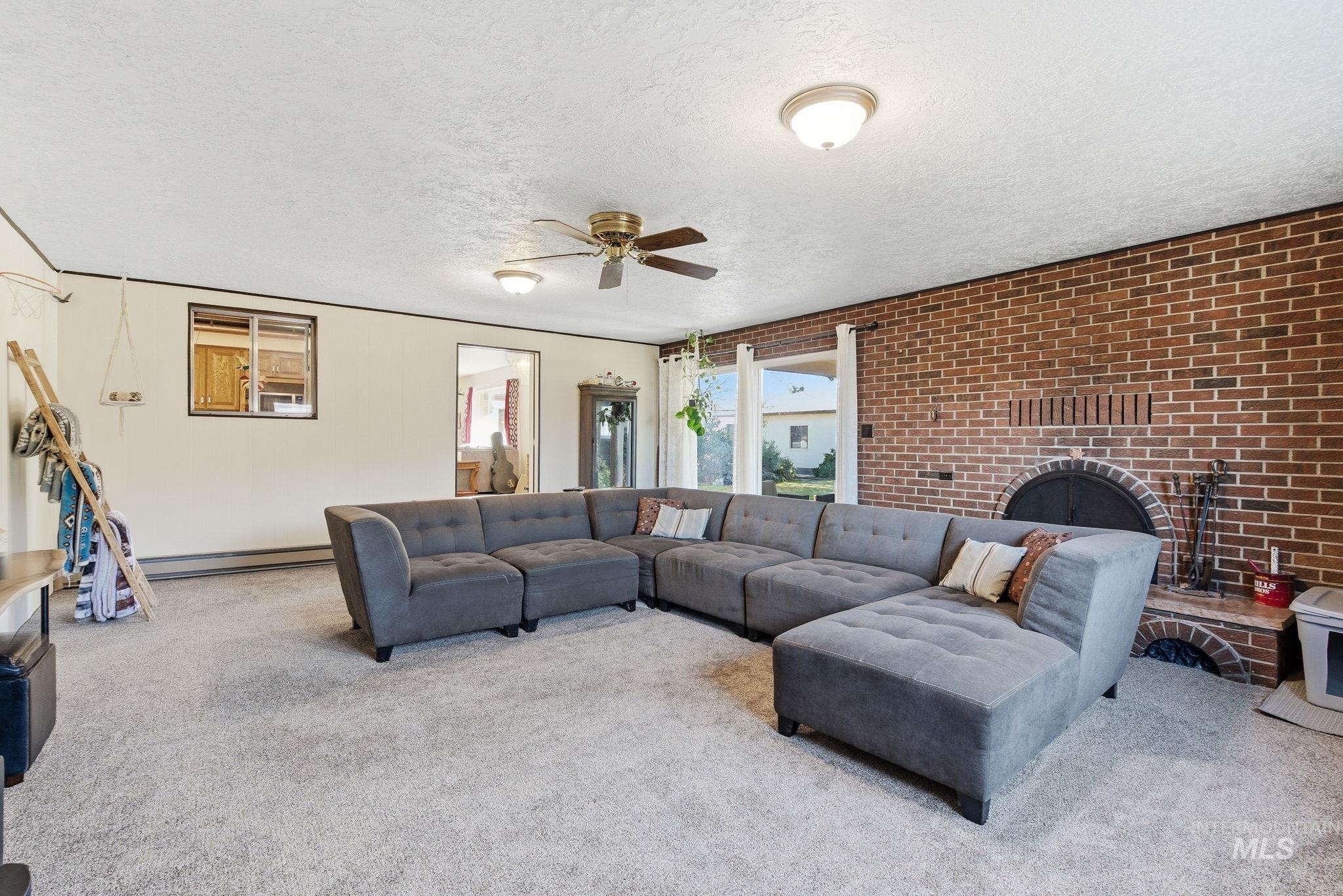12055 West McMillan Road Boise, ID 83713 - Photo 6 of 42 Carpeted living area with brick wall, a ceiling fan, a brick fireplace, a textured ceiling, and a baseboard radiator