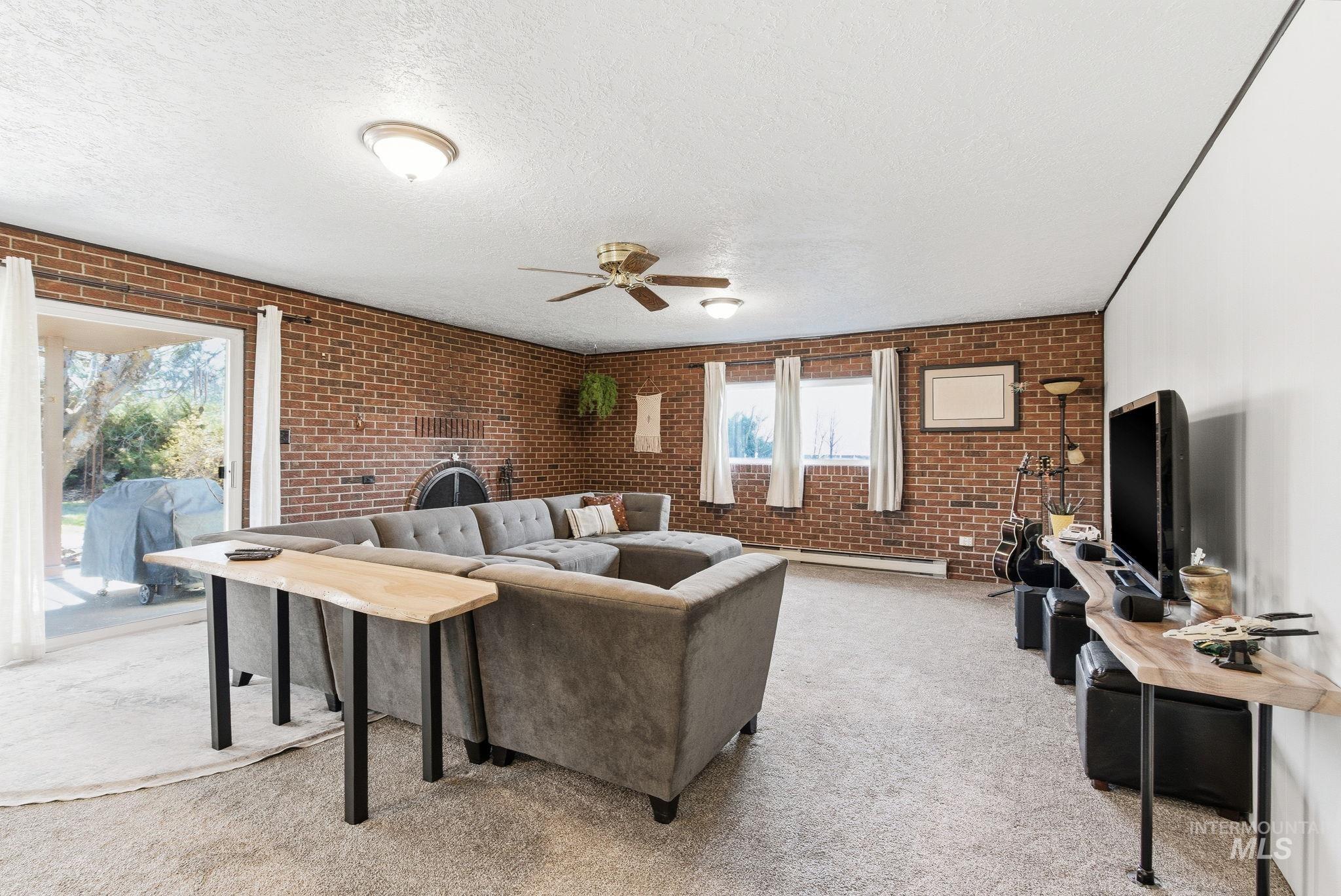 12055 West McMillan Road Boise, ID 83713 - Photo 7 of 42 Living room featuring brick wall, a ceiling fan, light carpet, a textured ceiling, and baseboard heating