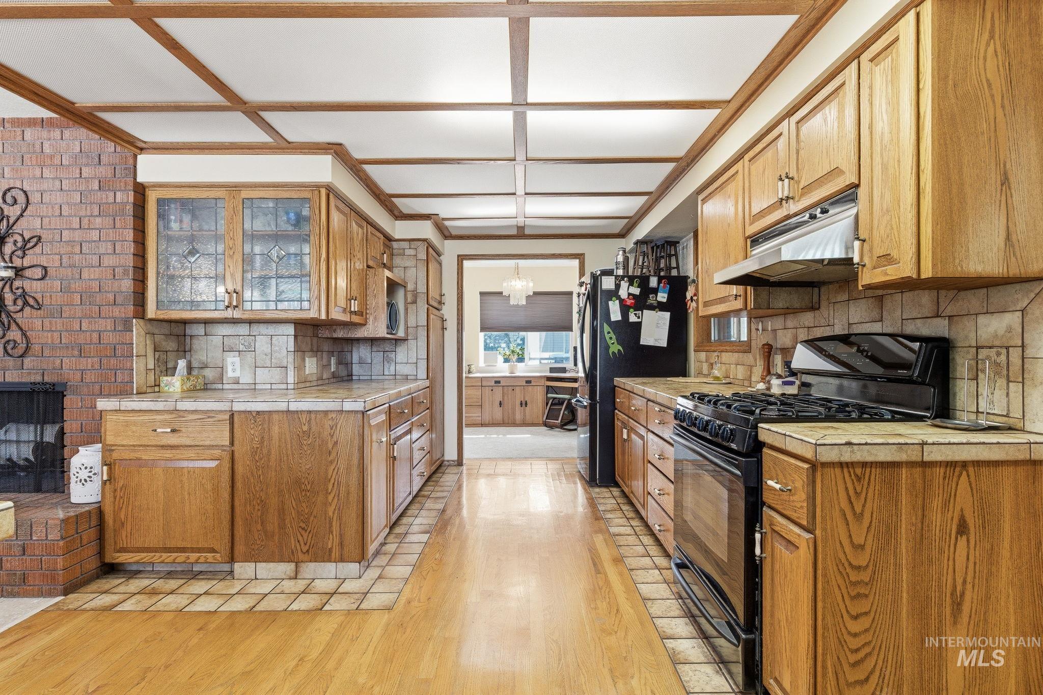 12055 West McMillan Road Boise, ID 83713 - Photo 9 of 42 Kitchen with black gas stove, light wood finished floors, a fireplace, and decorative backsplash