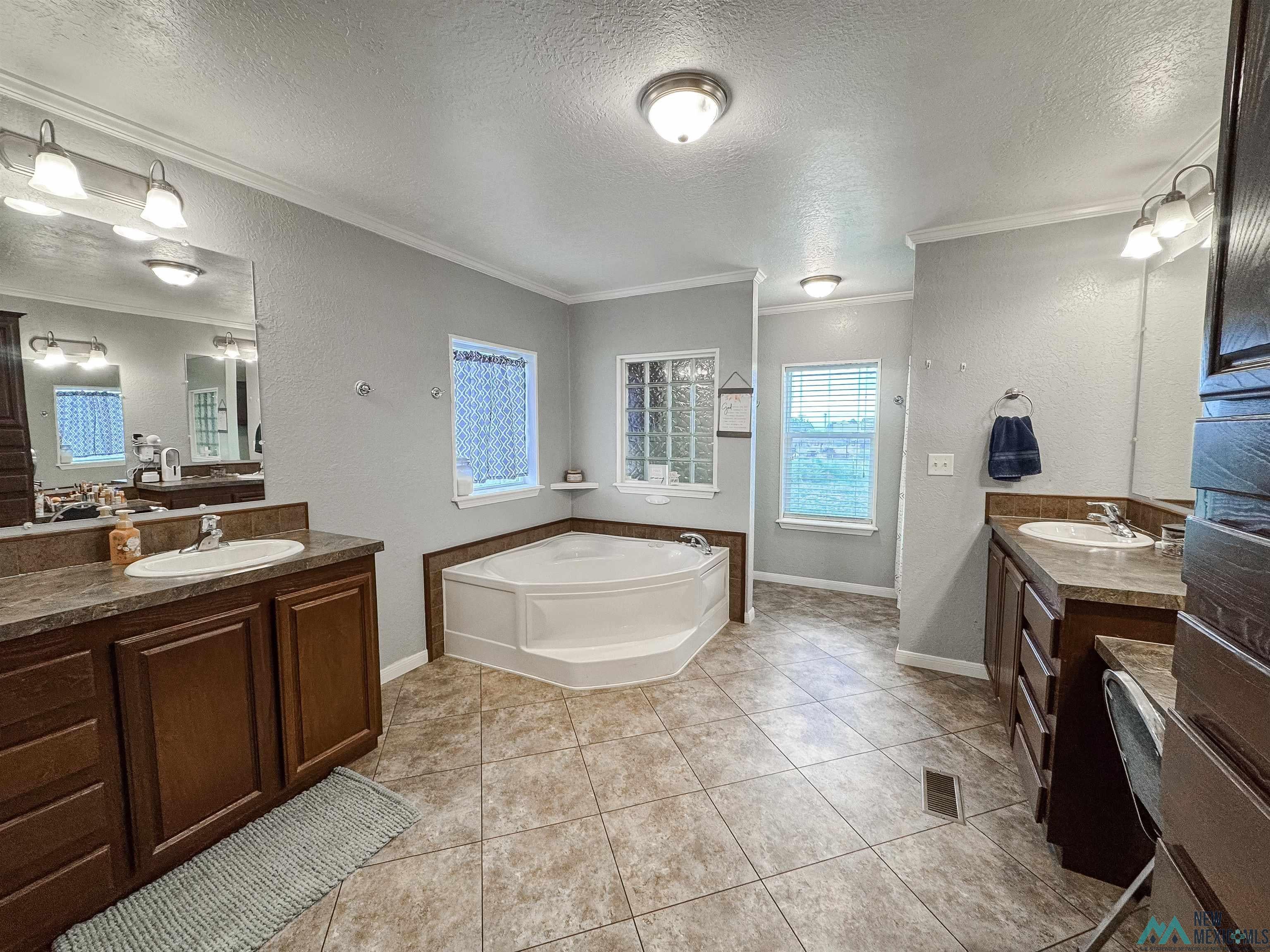 309 Crossbow Road Artesia, NM 88210 - Photo 18 of 31 Spacious bath featuring a corner soaking tub, dual vanities with integrated sinks, wood-finish cabinetry, and tiled flooring