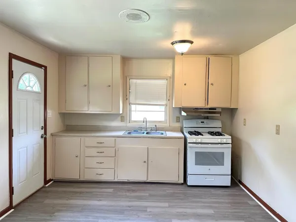 a kitchen with stainless steel appliances granite countertop a stove a sink and white cabinets with wooden floor next to windows