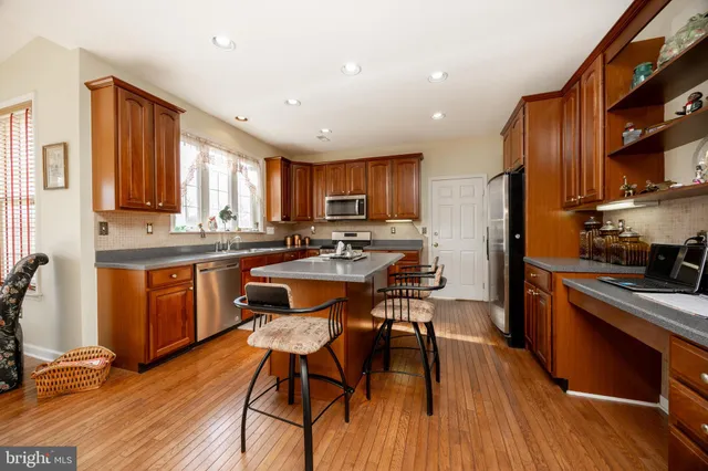 a kitchen with stainless steel appliances granite countertop wooden cabinets a refrigerator a stove a sink and a chairs