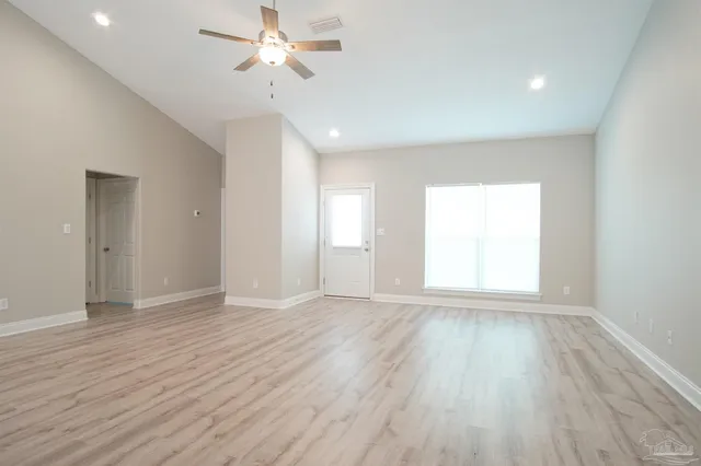 an empty room with wooden floor ceiling fan and windows