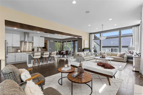 a living room with lots of furniture kitchen view and a large window