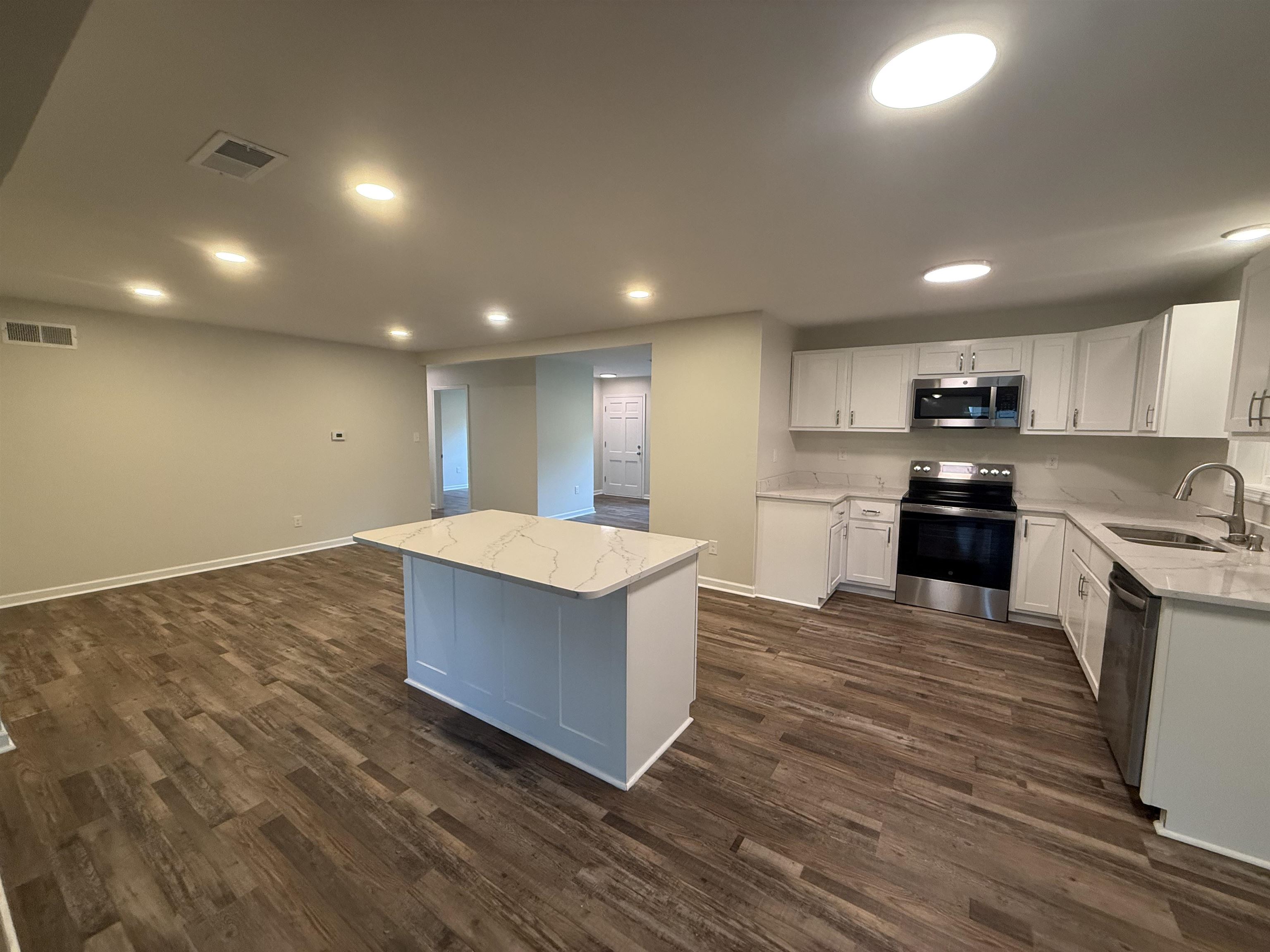 1835 Pleasant Grove Road Moscow, TN 38057 - Photo 10 of 34 Modern kitchen featuring a central island with a quartz-finish countertop, white cabinetry with silver hardware, and stainless steel appliances including a built-in microwave, range, and dishwasher
