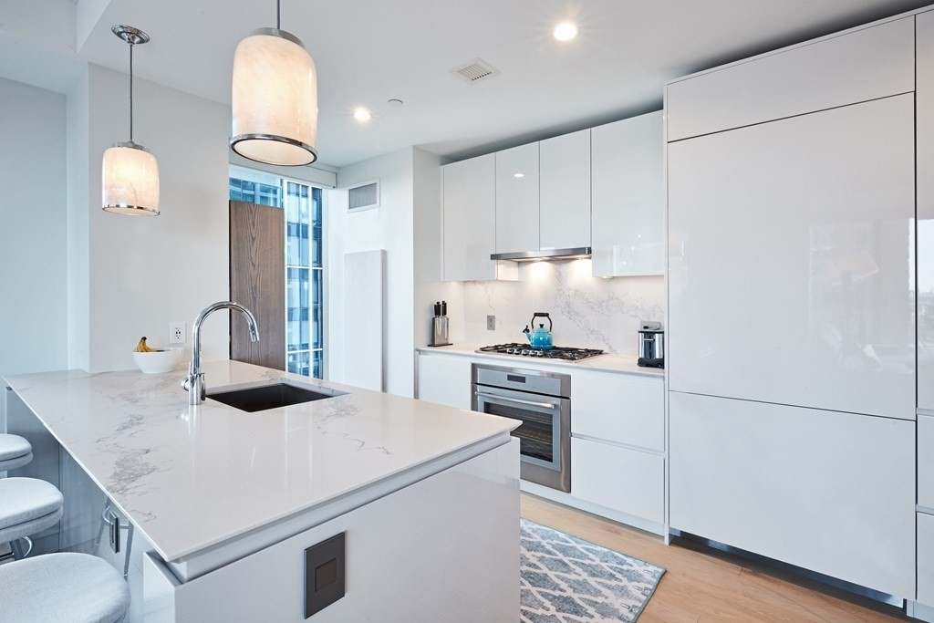 133 Seaport Boulevard, Unit 823 Boston, MA 02210 - Photo 4 of 30 a kitchen with stainless steel appliances a sink a stove a refrigerator a dining table and chairs with wooden floor