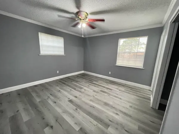 an empty room with wooden floor fan and windows
