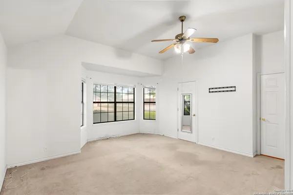 an empty room with chandelier fan and windows