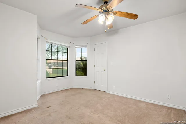 an empty room with chandelier fan and windows