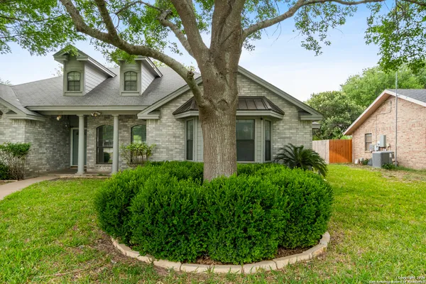 a view of a white house next to a yard with plants and large trees