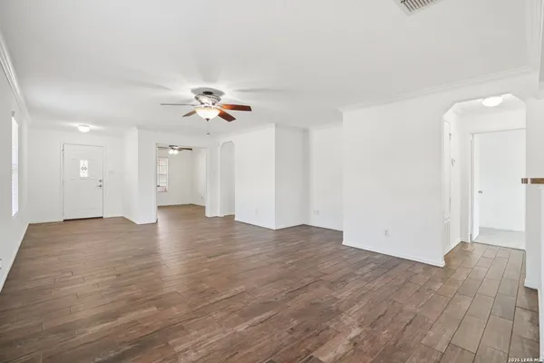 a view of an empty room with wooden floor and a ceiling fan