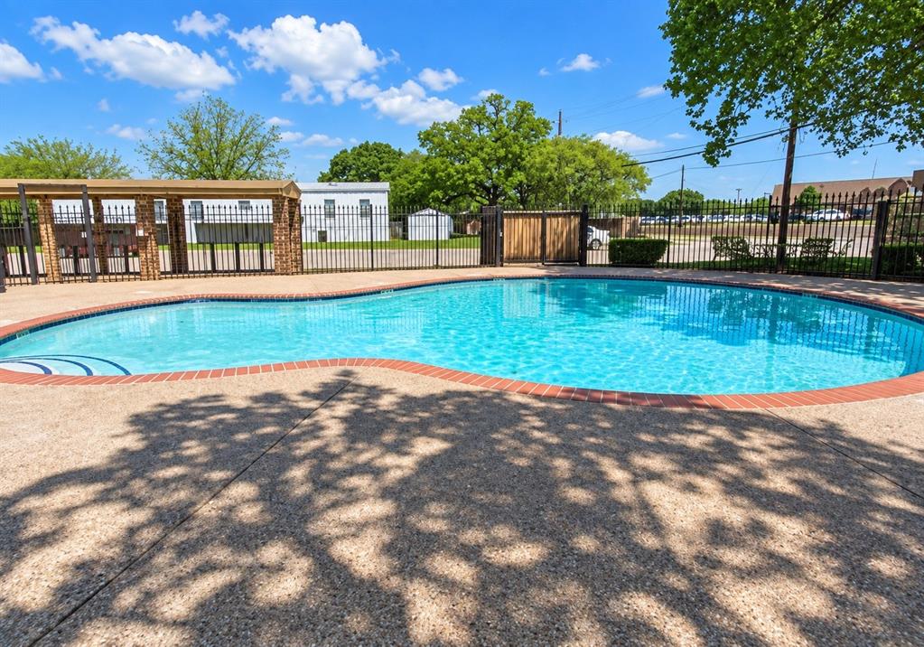 301 South Coppell Road, Unit 51 Coppell, TX 75019 - Photo 17 of 20 Curved swimming pool with a textured concrete deck, brick coping, and a surrounding black metal fence