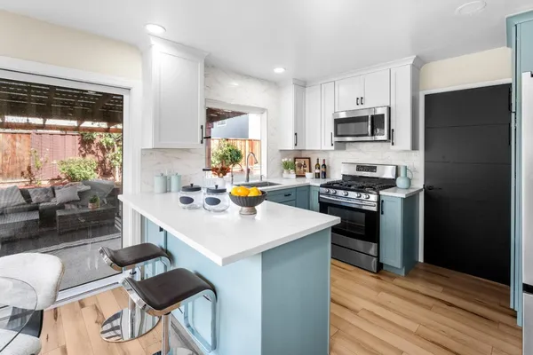 a kitchen with stainless steel appliances a sink a stove a refrigerator cabinets and a dining table with wooden floor