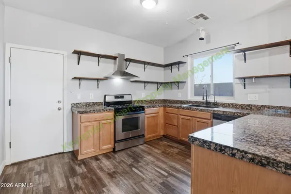 a view of an empty room and kitchen view with wooden floor