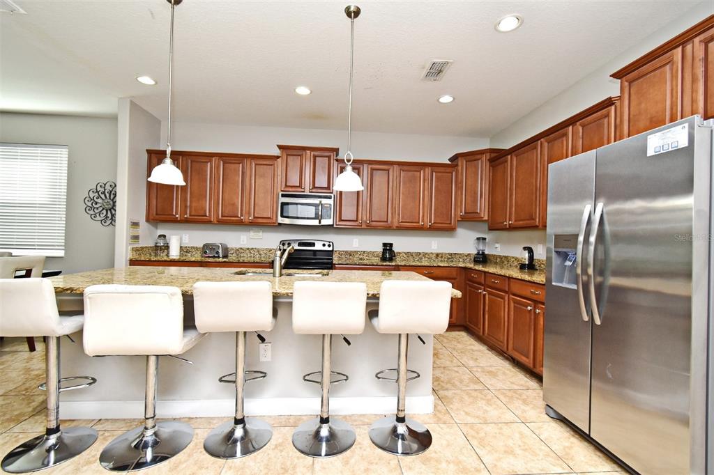 8878 Candy Palm Road Kissimmee, FL 34747 - Photo 14 of 70 a kitchen with stainless steel appliances kitchen island granite countertop a refrigerator and cabinets