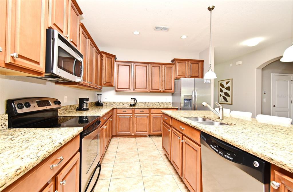 8878 Candy Palm Road Kissimmee, FL 34747 - Photo 16 of 70 a large kitchen with stainless steel appliances granite countertop a sink a stove and a wooden cabinets