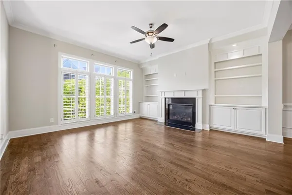 a view of a livingroom with wooden floor a ceiling fan and windows