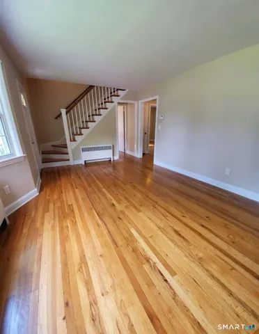 a view of an empty room with wooden floor and stairs