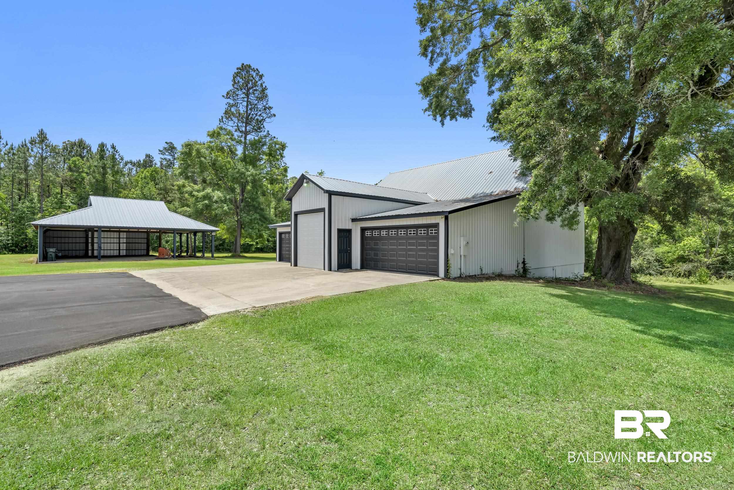 43199 Pine Grove Road Bay Minette, AL 36507 - Photo 13 of 71 Expansive paved and concrete driveway leading to a metal-sided building with multiple roll-up garage doors, a large attached garage door, and a separate open-sided metal structure