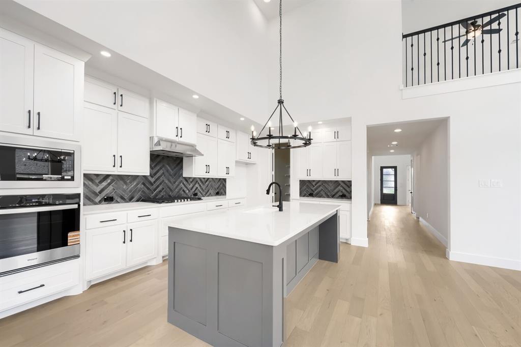 733 Red Cedar Road Haslet, TX 76052 - Photo 7 of 28 Contemporary kitchen featuring white cabinetry with black hardware, a herringbone pattern tile backsplash, and a central island with a light-toned countertop