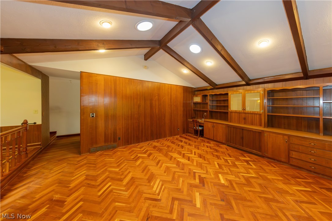 25001 Letchworth Road Beachwood, OH 44122 - Photo 16 of 50 Vaulted ceiling with exposed wood beams, wood-finish herringbone flooring, and extensive built-in wooden cabinetry featuring display shelves and storage
