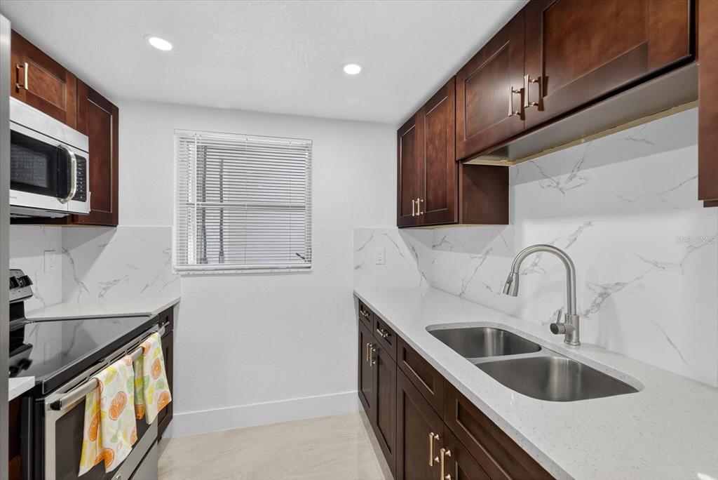 7421 Ashwood Drive Port Richey, FL 34668 - Photo 17 of 47 a kitchen with stainless steel appliances granite countertop a sink a stove top oven a refrigerator with wooden cabinets and floor