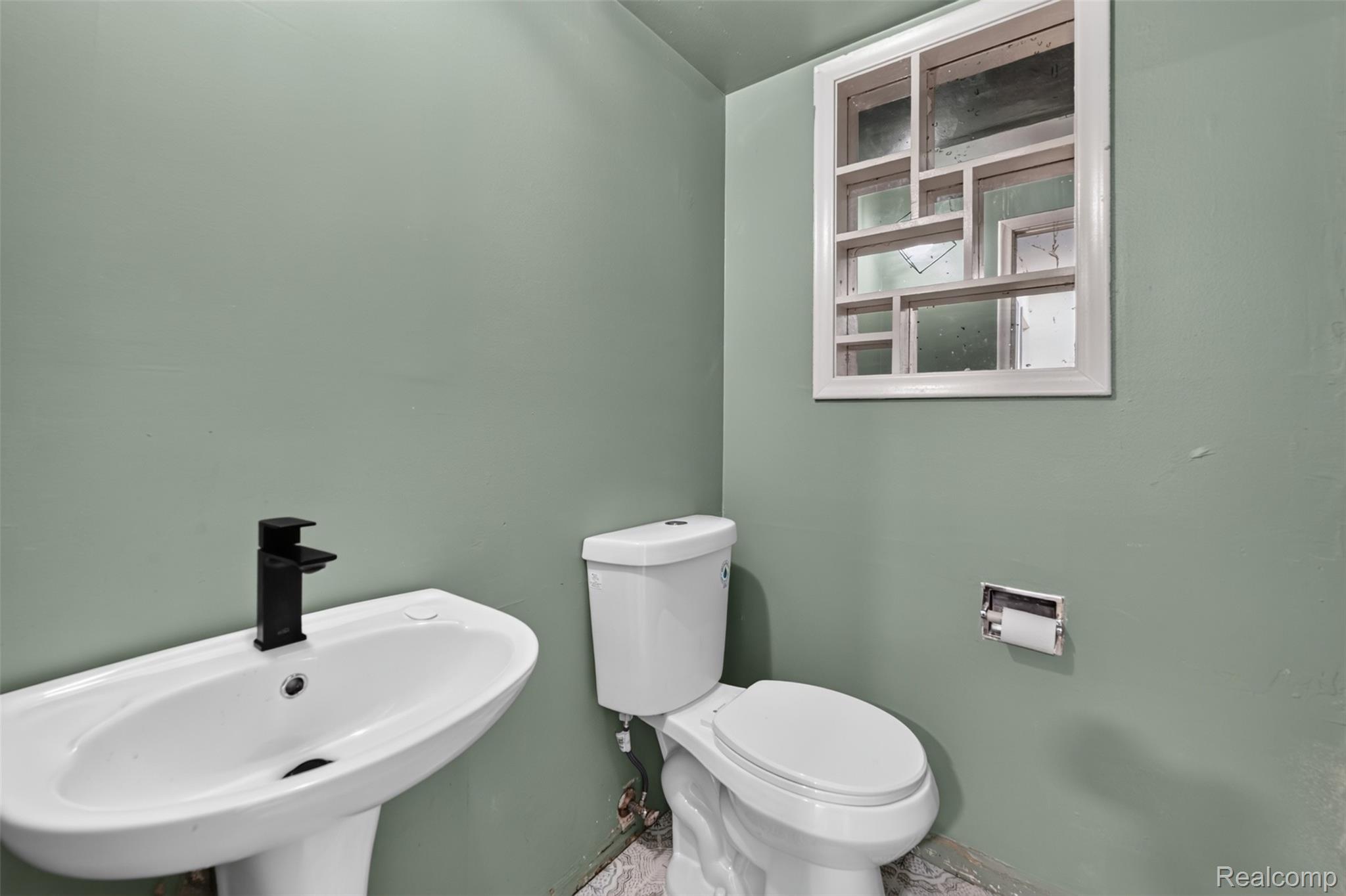 5457 Reid Road Swartz Creek, MI 48473 - Photo 17 of 51 White pedestal sink with a matte black faucet, complemented by a standard white toilet