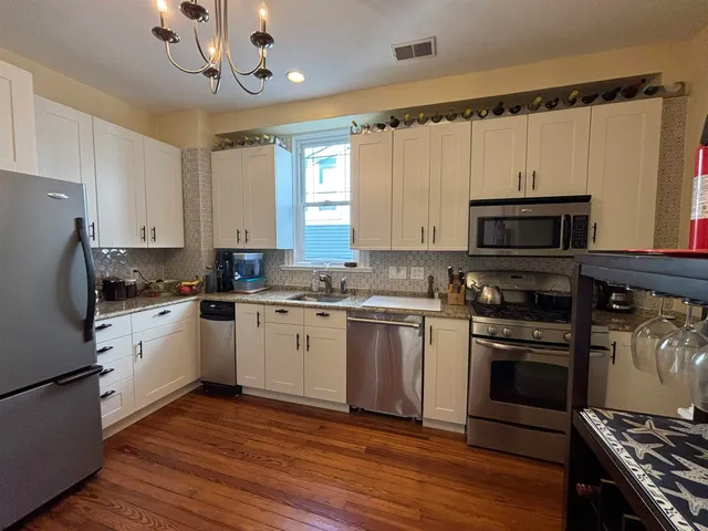 a kitchen with granite countertop a stove top oven a sink dishwasher a refrigerator and white cabinets with wooden floor