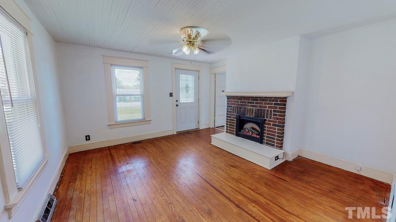 7089 Virgilina Road Roxboro, NC 27574 - Photo 2 of 28 an empty room with wooden floor fireplace and windows