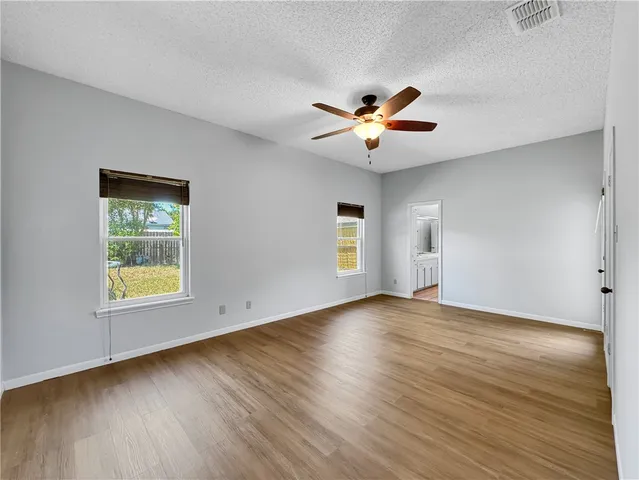 an empty room with wooden floor ceiling fan and windows